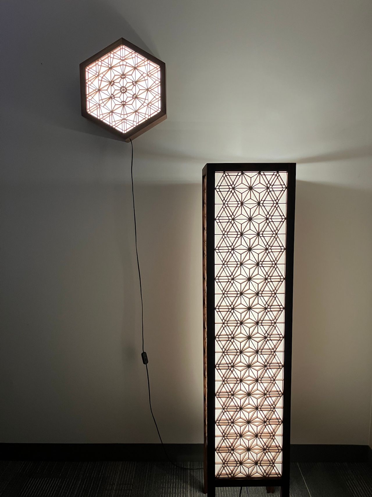 Tall goma floor lamp, lit, against a light wall